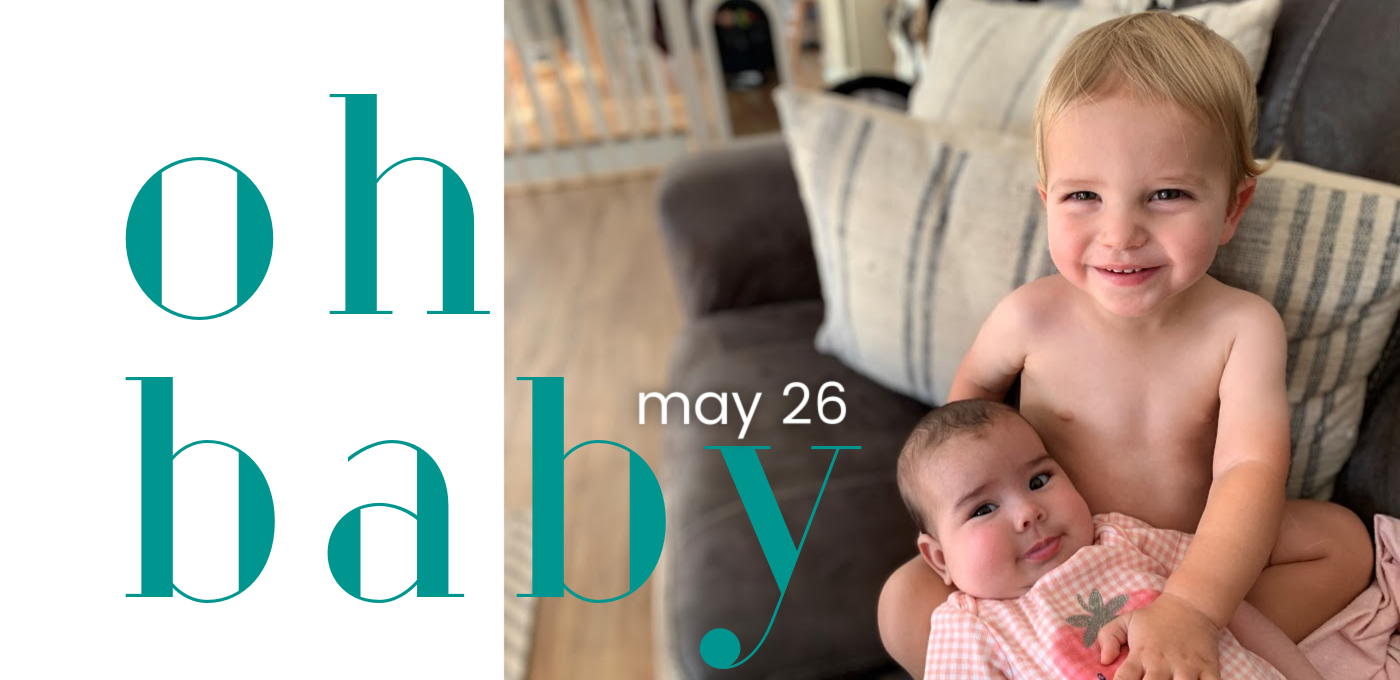 a toddler holding a baby on a grey couch with teal lettering