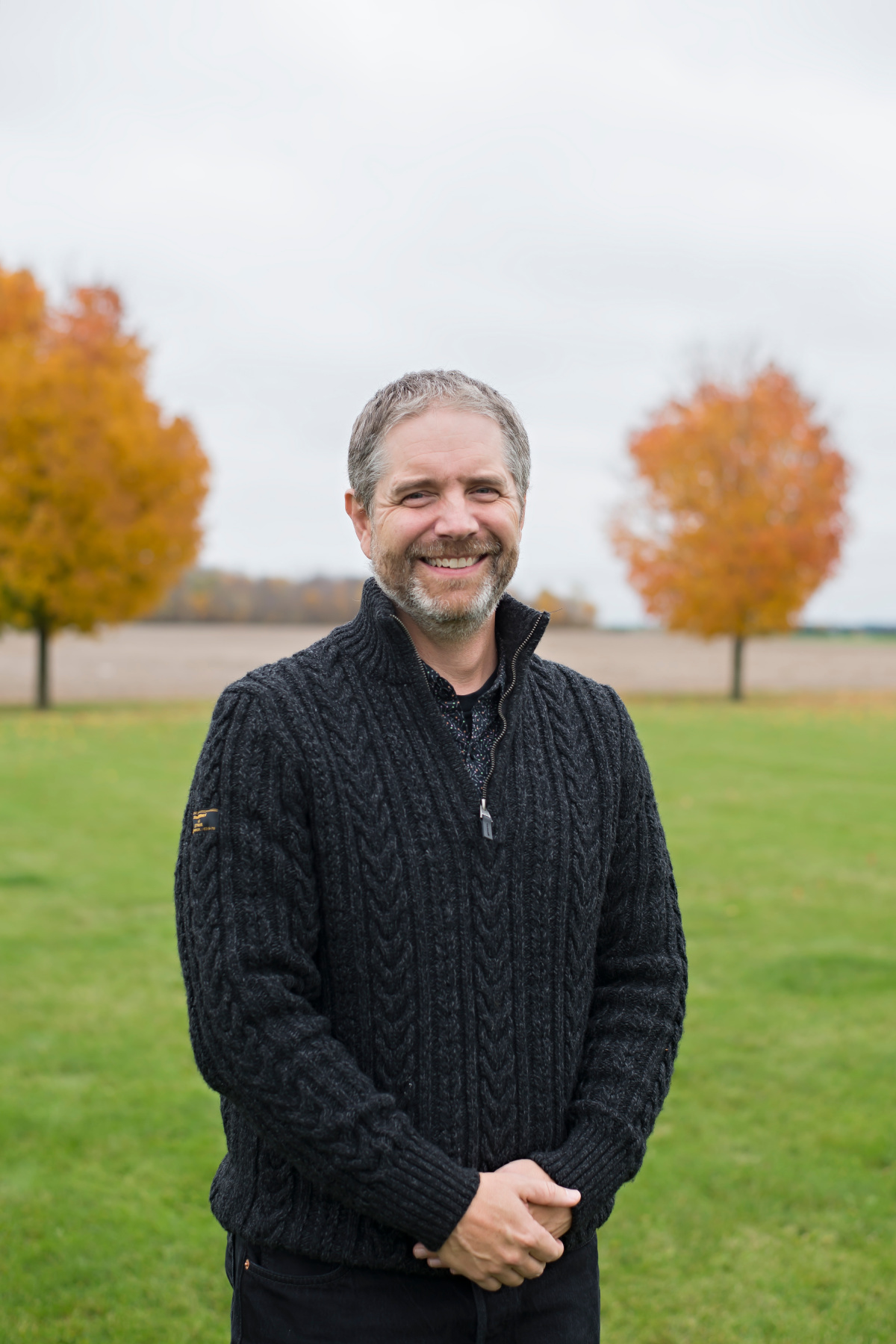 Man with black sweater in front of colourful fall tree