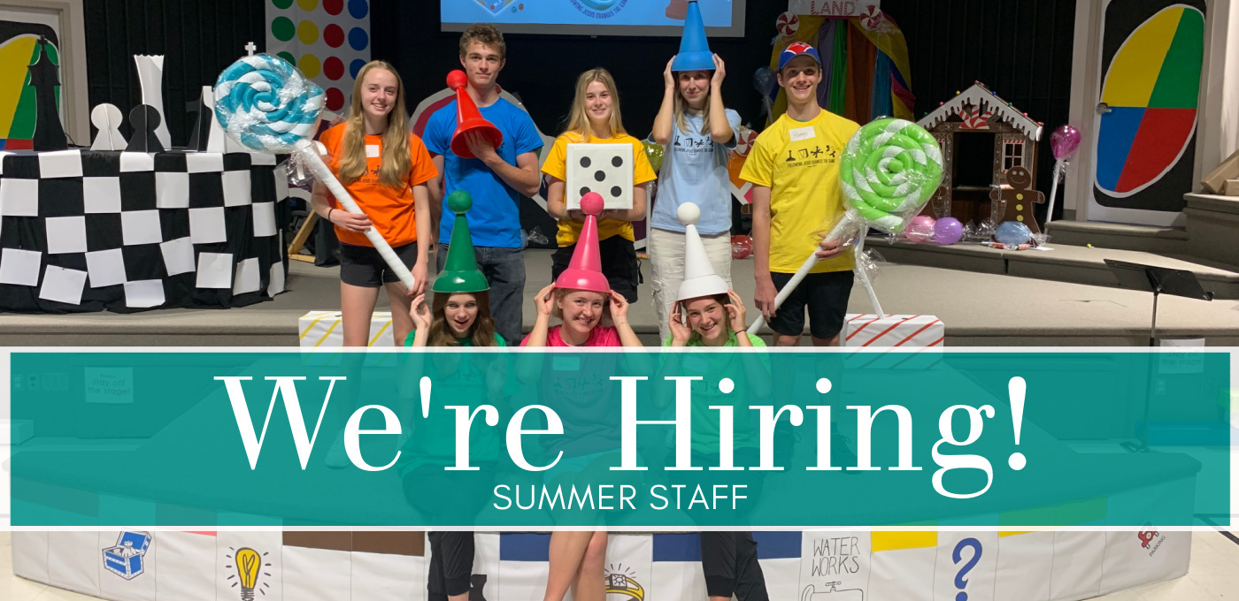 Group of youth sitting and standing on a stage with game pieces teal and white lettering